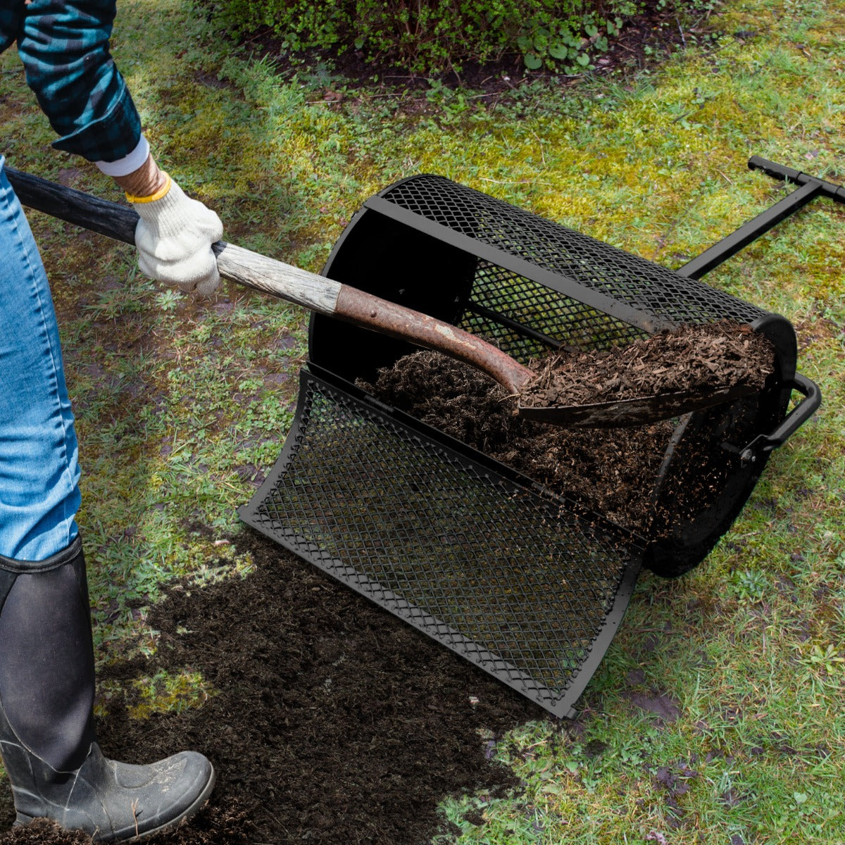 Schwarzer Garten Kompoststreuer mit runder Form, aus robustem Metall, der frischen Kompost gleichmäßig auf den Boden verteilt, umgeben von grünem Gras
