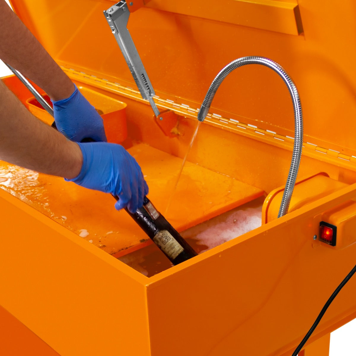 Teilewaschgerät in leuchtendem Orange mit einem Benutzer, der eine Flasche in die Waschlösung eintaucht, um sie gründlich zu reinigen