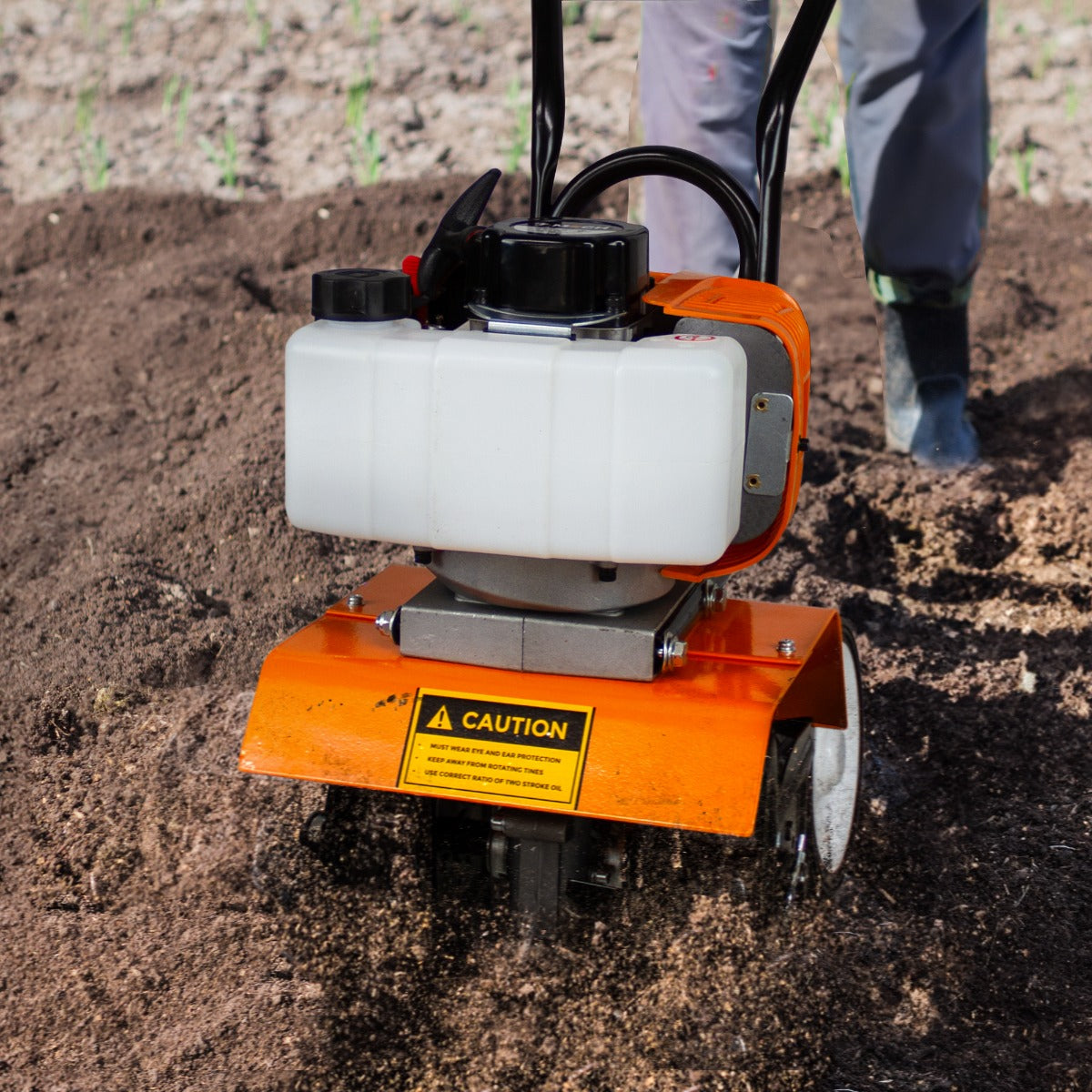 Die T-Mech Motorhacke in leuchtendem Orange mit schwarzem Motor und weißem Tank bearbeitet fruchtbaren Boden, ideal für Gartenarbeiten