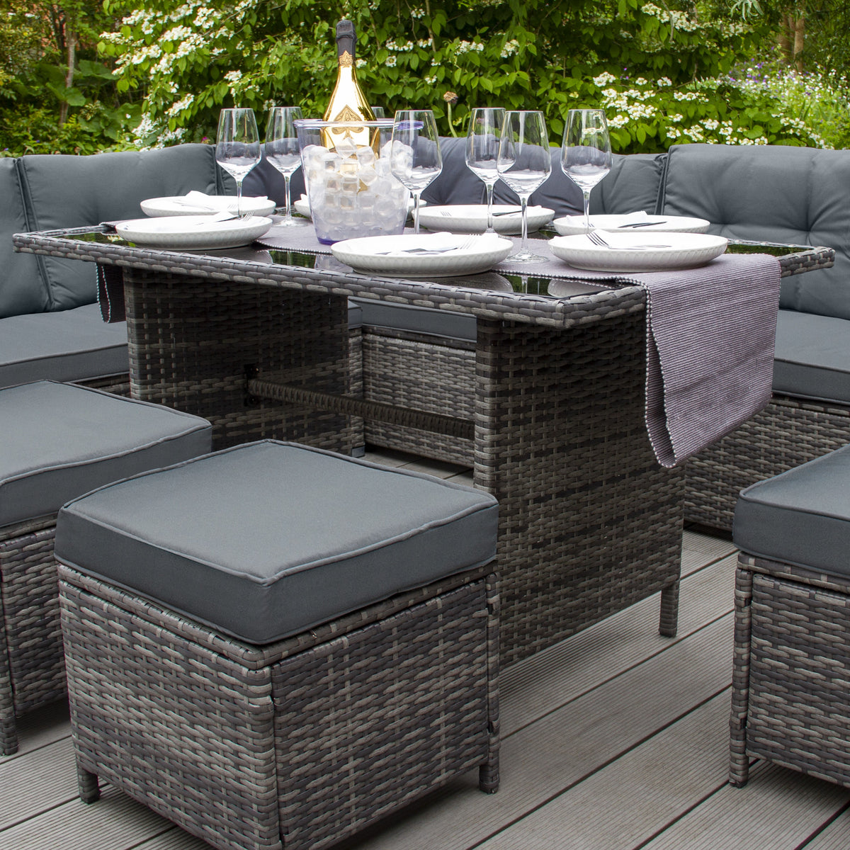 Schwarzes Polyrattan Gartenmöbel Set mit bequemen grauen Kissen, eleganter Glasplatte und stilvollen Accessoires auf einer Holzterrasse