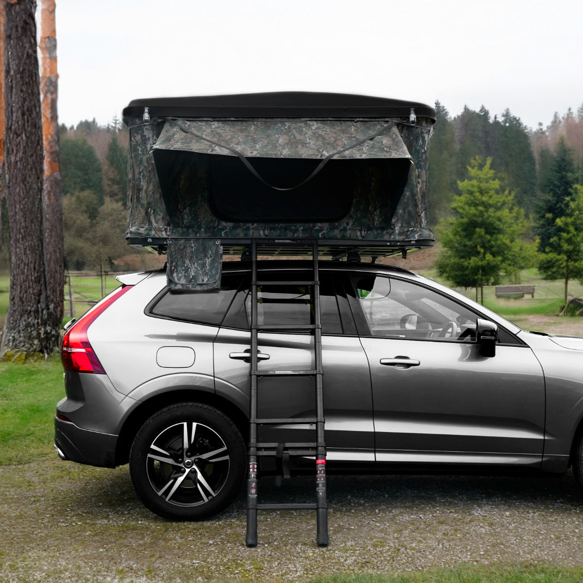 Dachzelt in Camouflage-Design auf einem grauen SUV, mit einer stabilen Leiter, umgeben von Bäumen und Wiese im Hintergrund