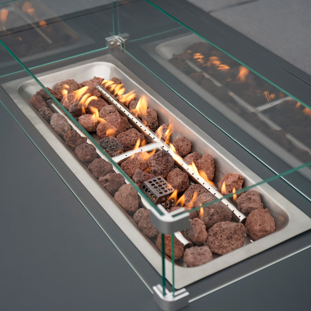 Modulares Gartenlounge-Set mit eleganter Feuerstelle, umgeben von glatten Steinen, in einem modernen, minimalistischen Design aus Edelstahl und Glas