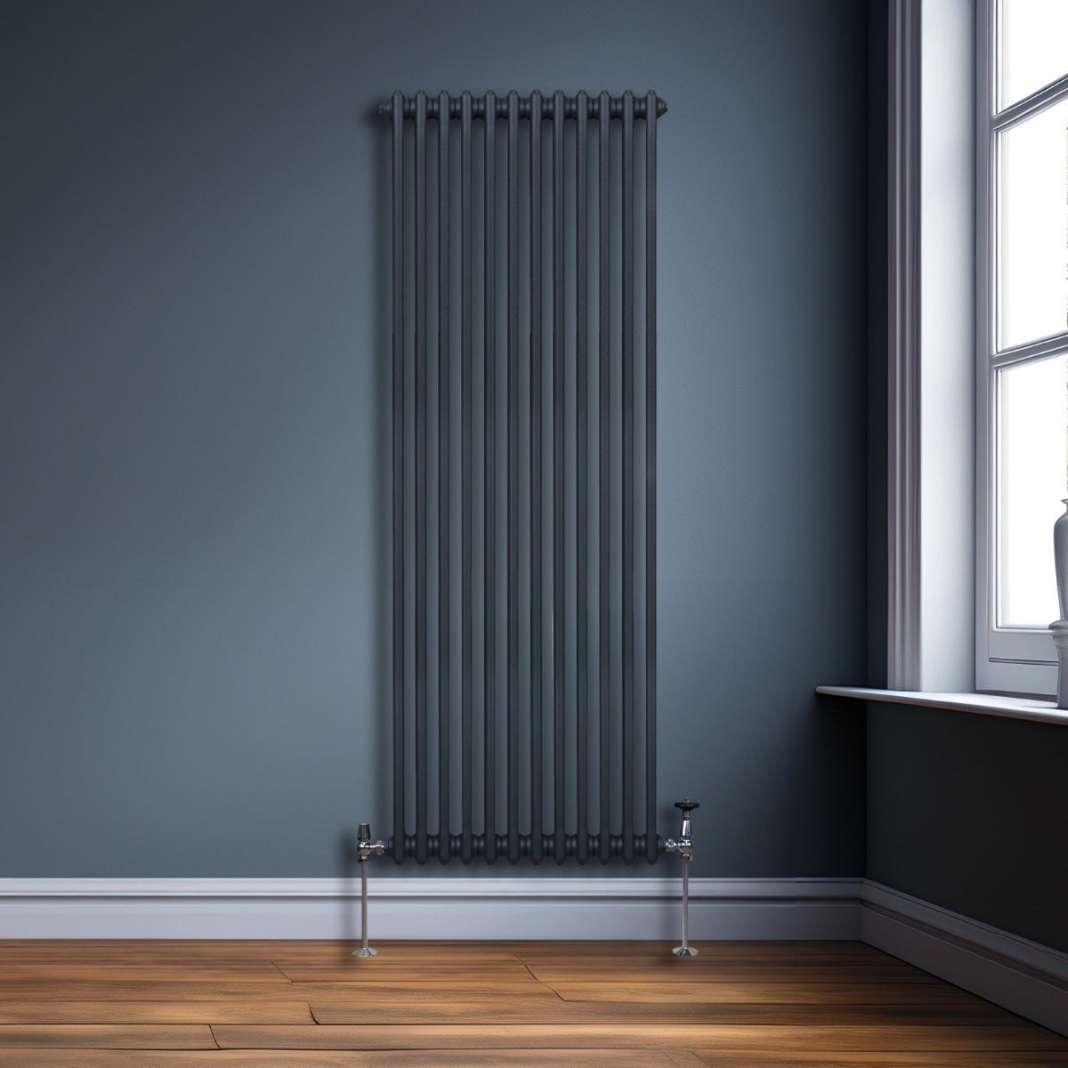 Traditioneller 2-Spalten-Heizkörper in Anthrazitgrau, 1800 x 562 mm, mit vertikalen Röhren und glänzenden Metallfüßen, vor einer blauen Wand und Holzfußboden