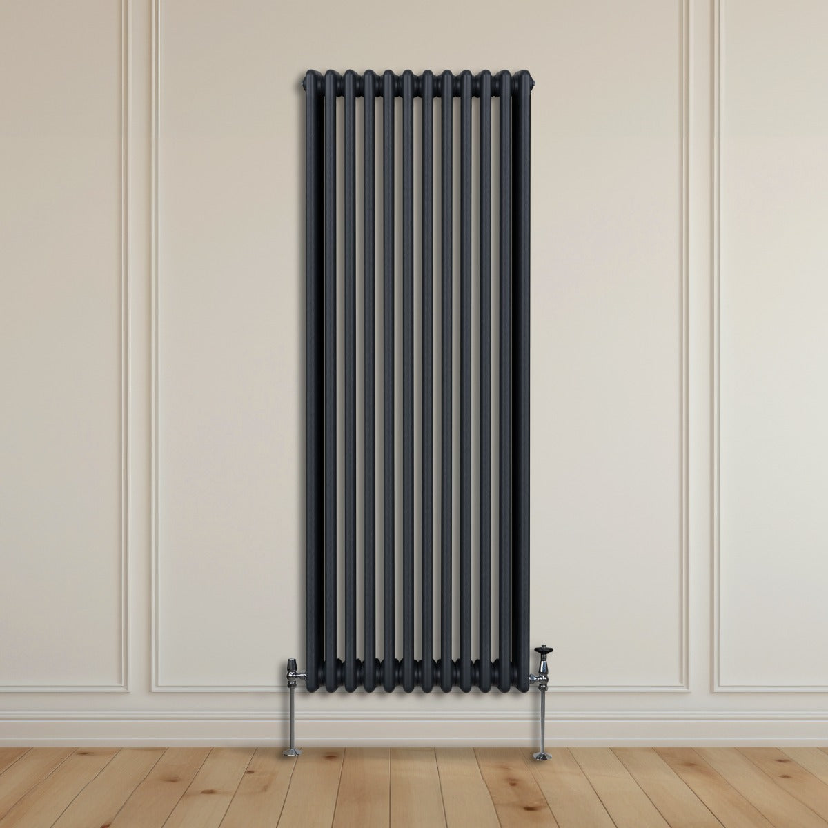 Traditioneller 3-Spalten-Heizkörper in Anthrazitgrau, vertikal montiert an einer hellen Wand, mit glänzenden Metallfüßen und Holzfußboden darunter