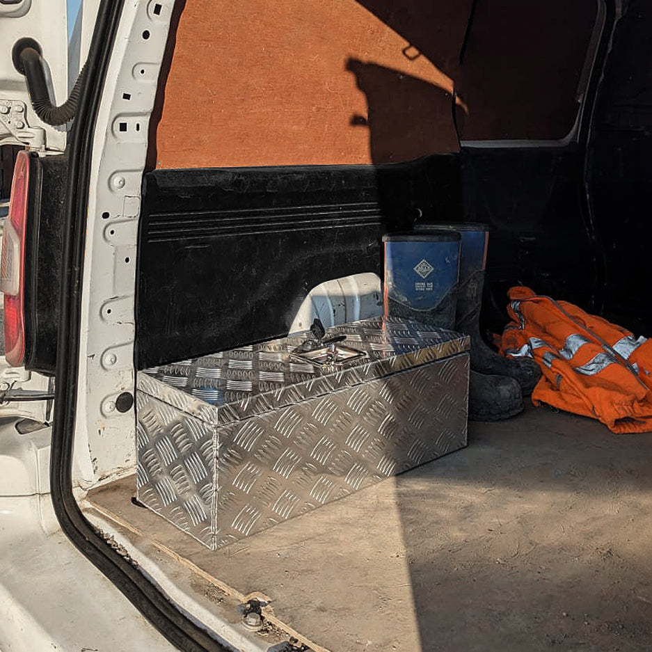Aluminium-Werkzeugkasten in silberner Rautenstruktur, 35L, steht im Kofferraum eines Fahrzeugs, umgeben von Arbeitskleidung und Werkzeugen