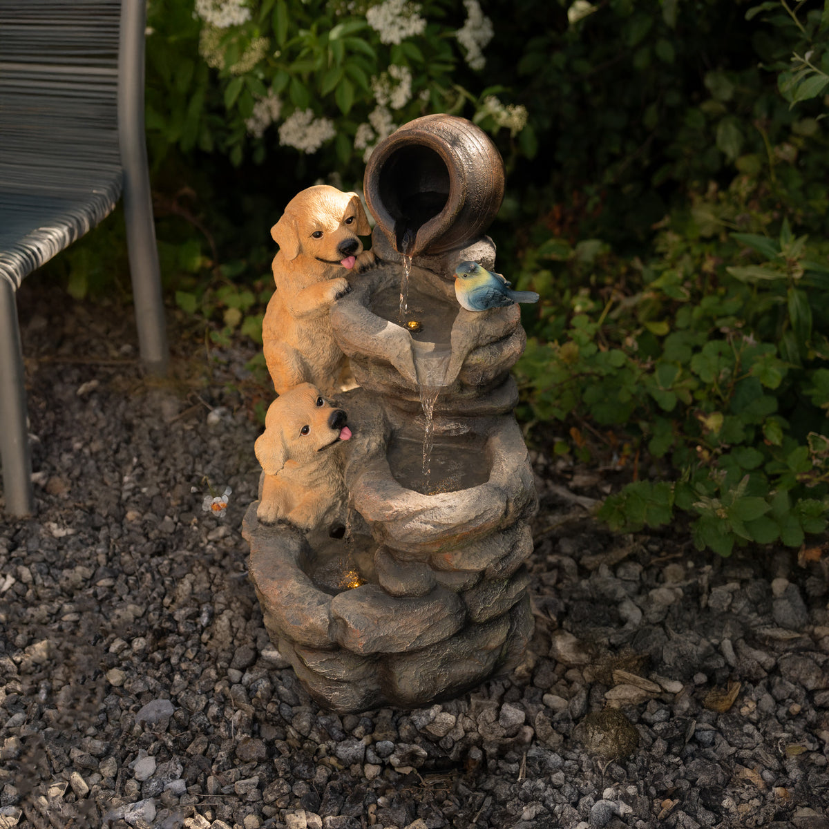 Eine elektrische Wasseranlage mit zwei niedlichen Hundewelpen, die aus einem Topf trinken, umgeben von Steinen und Pflanzen im Garten