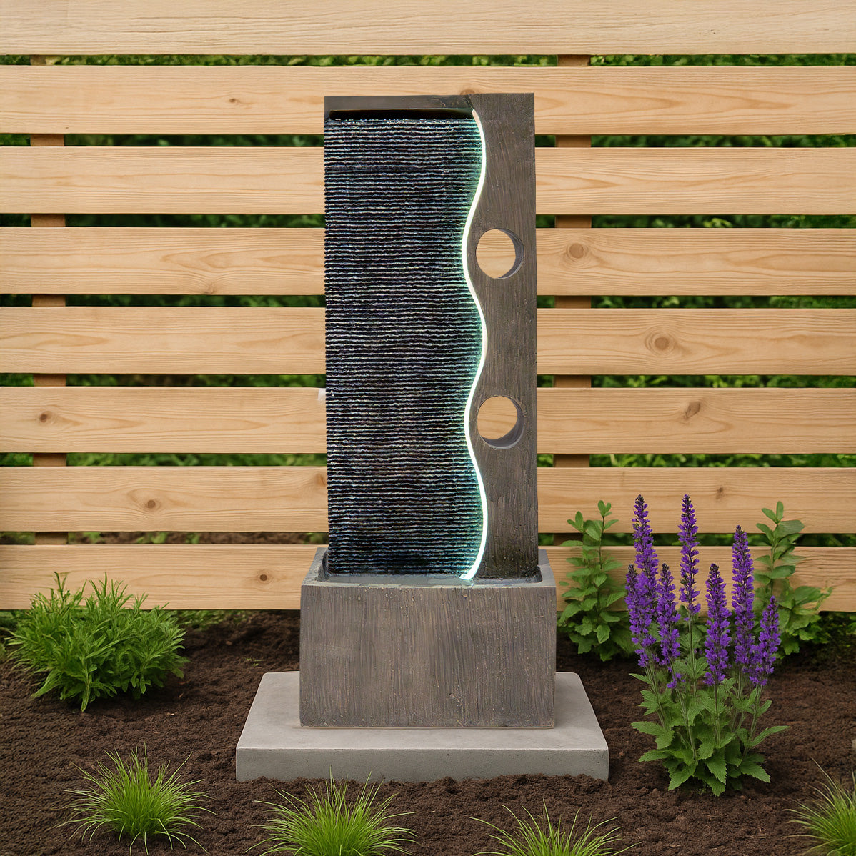 Moderne elektrische Wasseranlage "Harmony Falls" mit sanft fließendem Wasser, beleuchtetem Wellenmuster und grauem Beton, umgeben von lila Blumen und grünem Gras