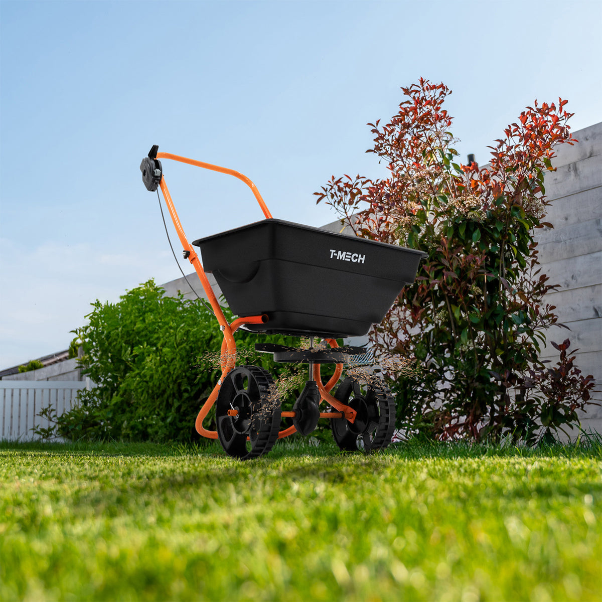 Rasennivellierer und Rotationsstreuer von T-Mech in Orange mit schwarzem Behälter, robusten Rädern und ergonomischem Griff, ideal für Rasenpflege