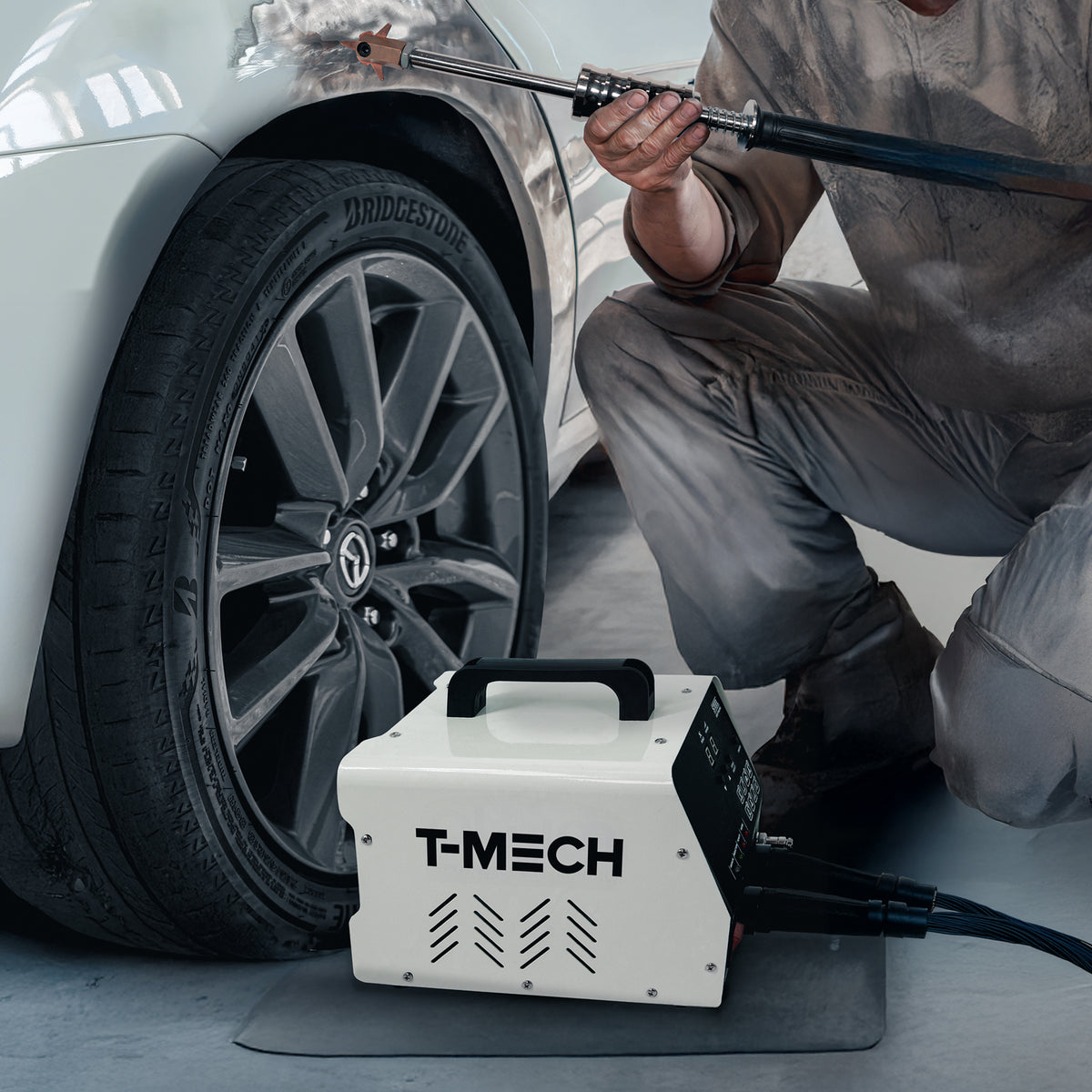 Ausbeulenzieher-Maschine in Weiß mit schwarzem Griff, neben einem Auto mit einem reparierten Kotflügel und einem Mechaniker, der das Werkzeug hält