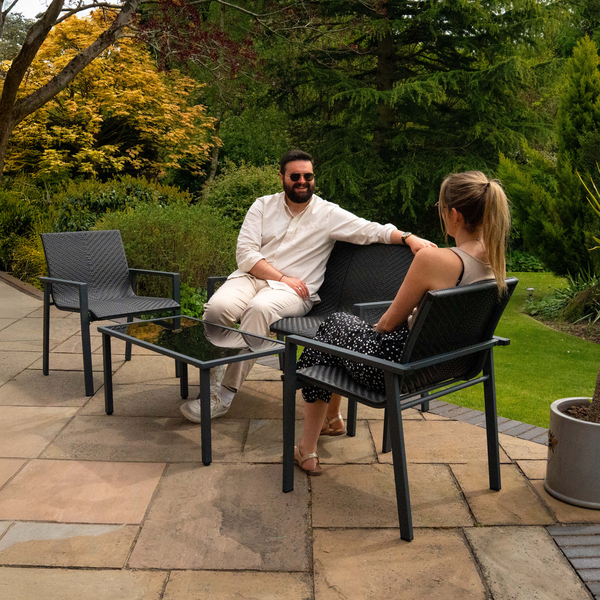 Schwarzes Rattan Terrassenmöbel Set mit zwei Stühlen und einem Tisch, ideal für entspannte Stunden im Freien, umgeben von grüner Natur