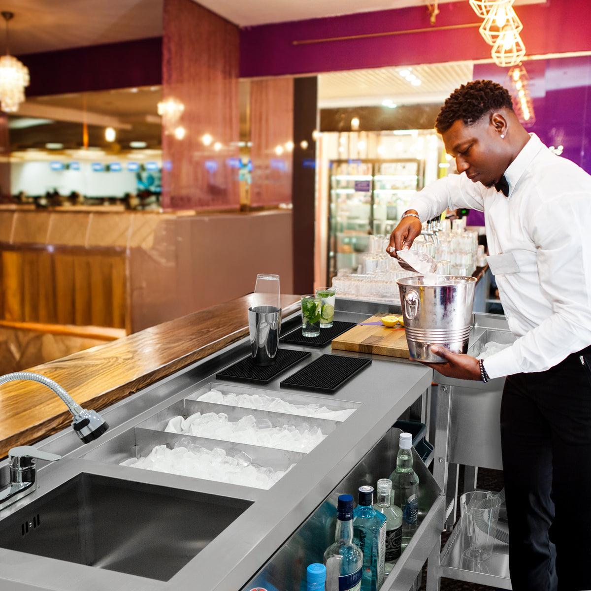 Modulare Cocktailbar-Station mit Eisbrunnen, eleganter Barkeeper in weißem Hemd, gefüllte Eisbehälter, stilvolle Getränke und Gläser