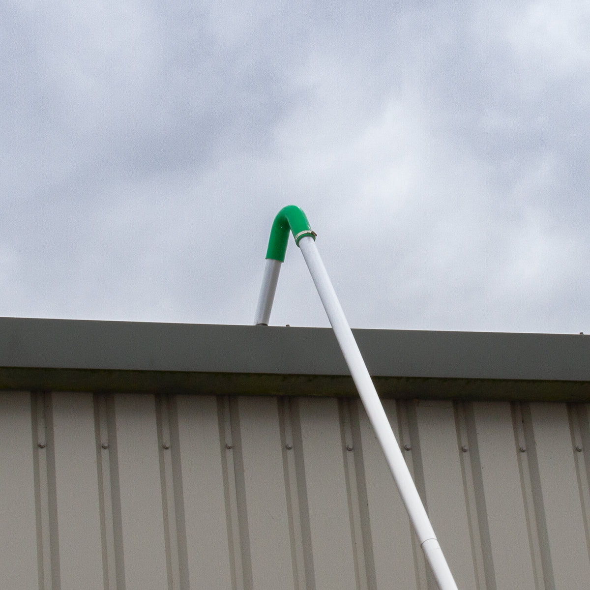Grüne Dachrinnen-Saugstange aus robustem Kunststoff, die an einer grauen Metallwand befestigt ist, mit einem klaren, wolkigen Himmel im Hintergrund