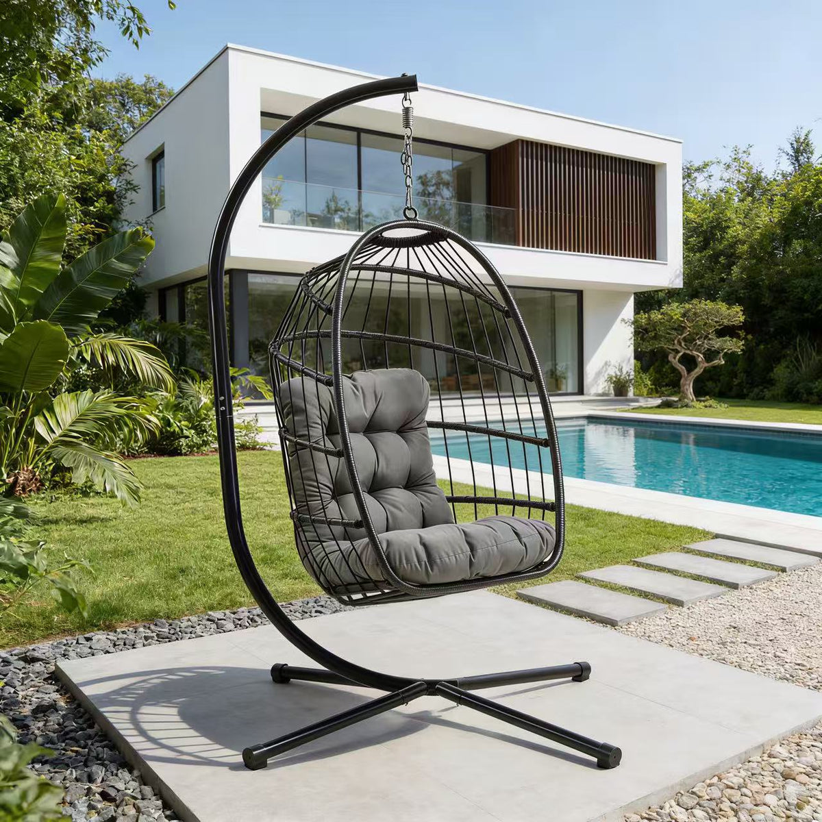 Schwarzer Rattan Hängesessel in Eiform mit grauem Kissen, elegant aufgehängt an einem stabilen Gestell, umgeben von einem modernen Garten und Pool