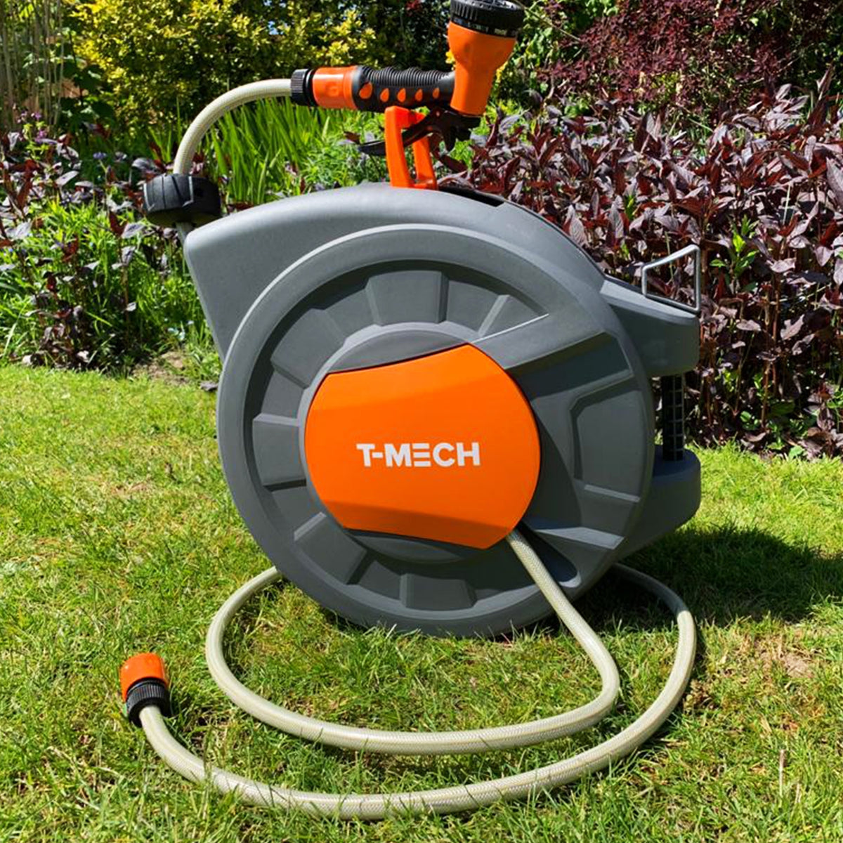 Graue Schlauchtrommel mit orangefarbenen Akzenten, ausgestattet mit einem Gartenschlauch und einer Spritzdüse, auf grünem Rasen platziert