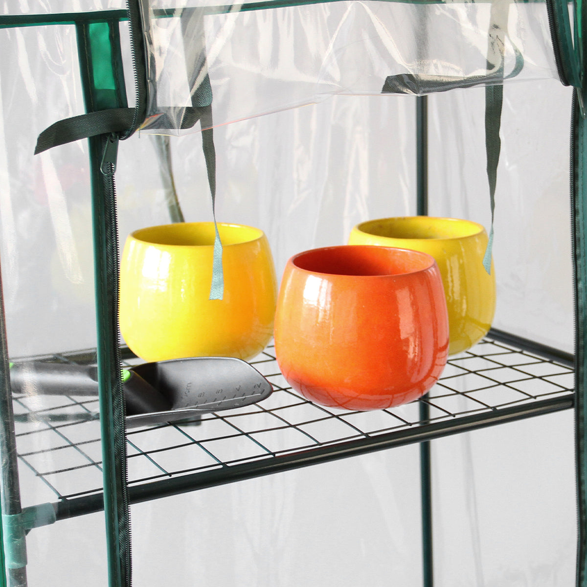 Mini-Gewächshaus mit transparenter Kunststoffabdeckung, vier Regalen und bunten Töpfen in Gelb, Orange und Rot, ideal für Pflanzenzucht
