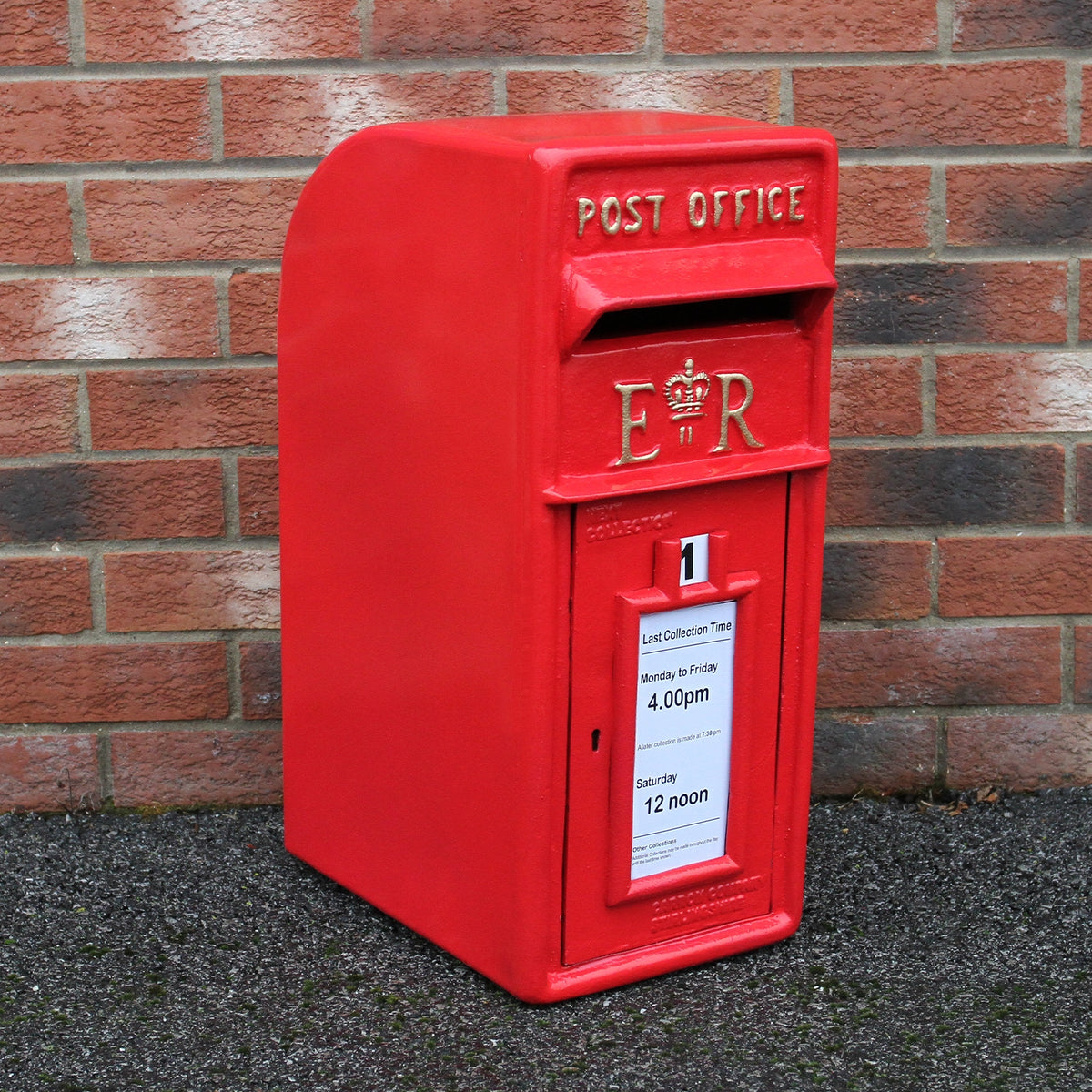 Roter Briefkasten mit Bodenständer, glänzende Oberfläche, klassische Form, mit Post Office Aufschrift und abnehmbaren Sammelzeiten auf einem Ziegelstein-Hintergrund