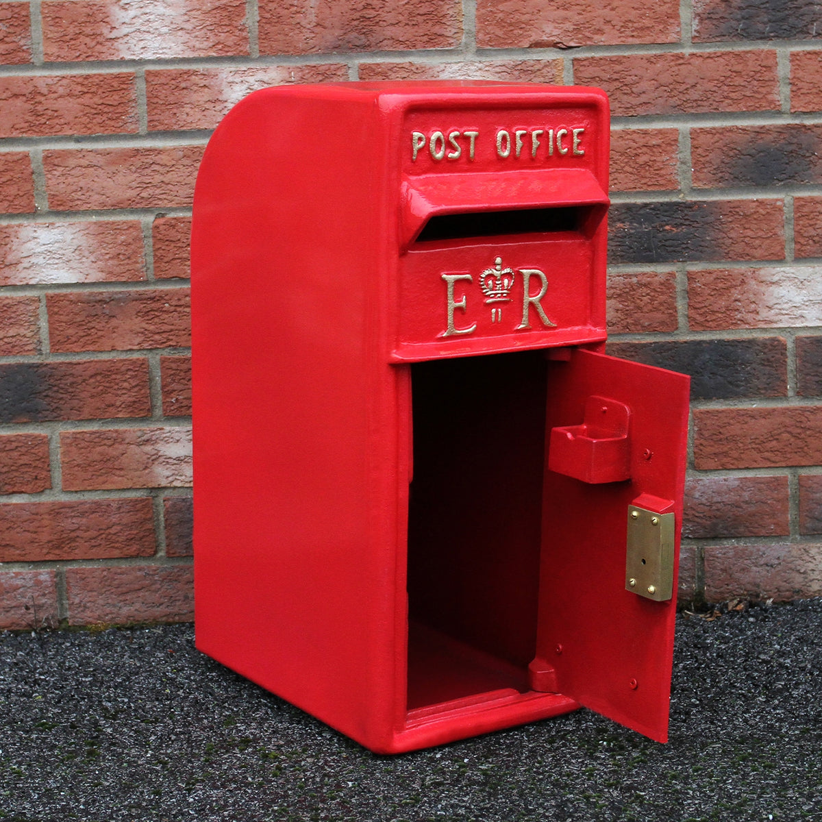 Roter Briefkasten mit Bodenständer, glänzende Oberfläche, goldene Buchstaben "ER" und "POST OFFICE", offen für den Briefversand, vor einer Ziegelwand