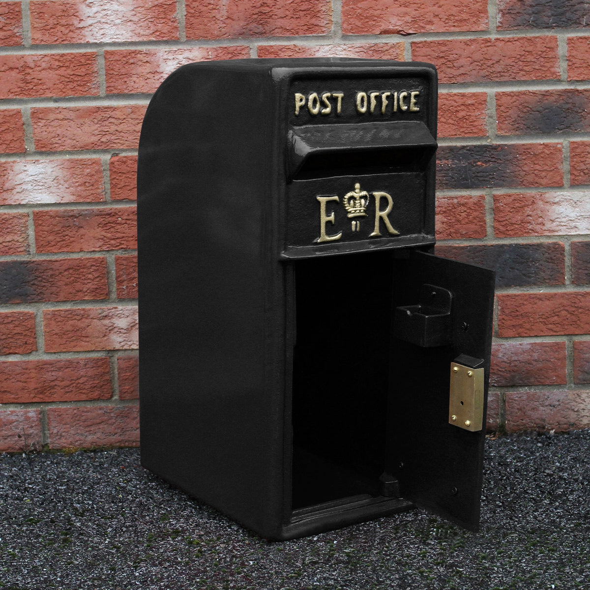 Schwarzer Briefkasten mit Bodenständer, glänzender Oberfläche, goldene Schriftzüge "POST OFFICE" und "ER", klassisches Design vor roter Ziegelwand