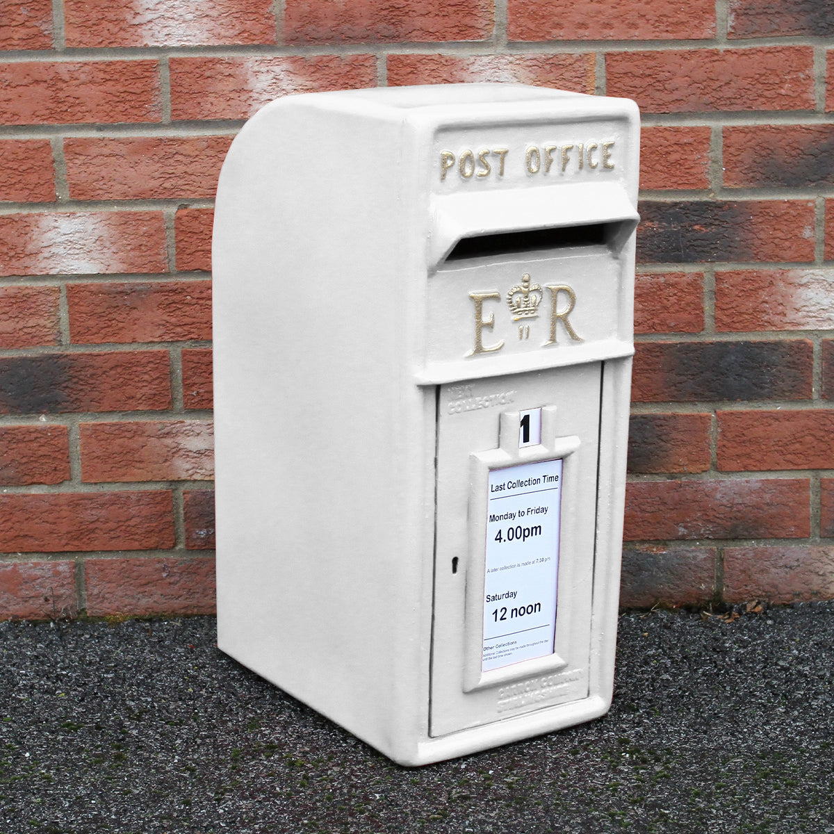 Weißer Briefkasten mit Bodenständer, aus robustem Material, mit königlichem Emblem und klar lesbarem Abholzeit-Schild, vor einer Ziegelmauer platziert