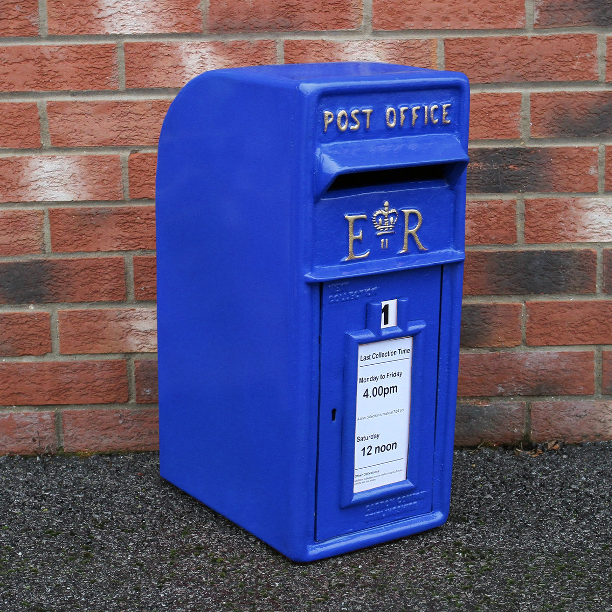 Blauer Briefkasten im schottischen Stil mit königlichem Wappen, rechteckiger Form und glatter Oberfläche, vor einer roten Ziegelwand platziert