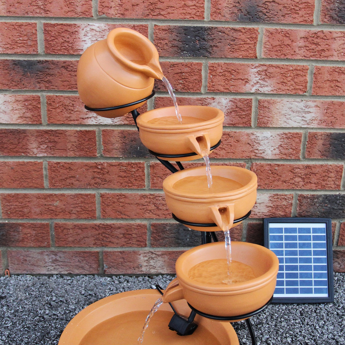 Terracotta Solar Kaskadenbrunnen mit vier Schalen, die Wasser in sanften Strahlen fließen lassen, vor einer roten Ziegelwand platziert