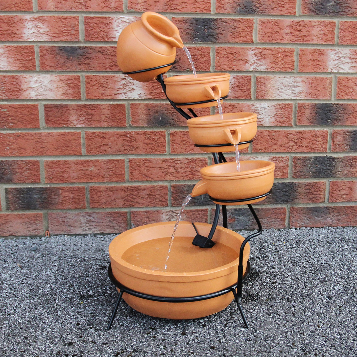 Terracotta Solar Kaskadenbrunnen mit fünf Töpfen, die Wasser in eine große Schale leiten, umgeben von grauem Kies und einer Ziegelmauer