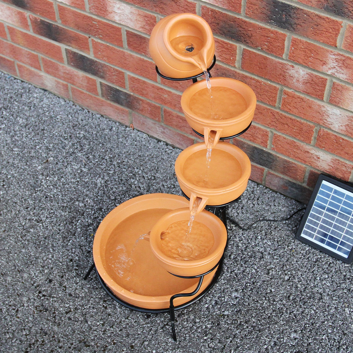 Terracotta Solar Kaskadenbrunnen mit vier Schalen, Wasser fließt sanft von oben nach unten, umgeben von einem stabilen Metallgestell und einem Solarpanel
