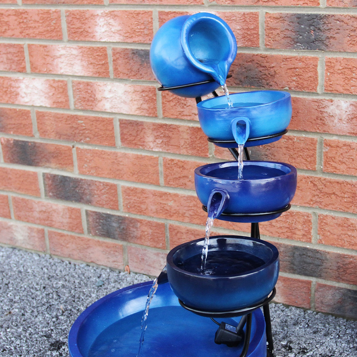 Blauer Solar Kaskadenbrunnen mit fünf Schalen, die Wasser in sanften Strömen abgeben, auf einem stabilen schwarzen Gestell vor einer roten Ziegelwand