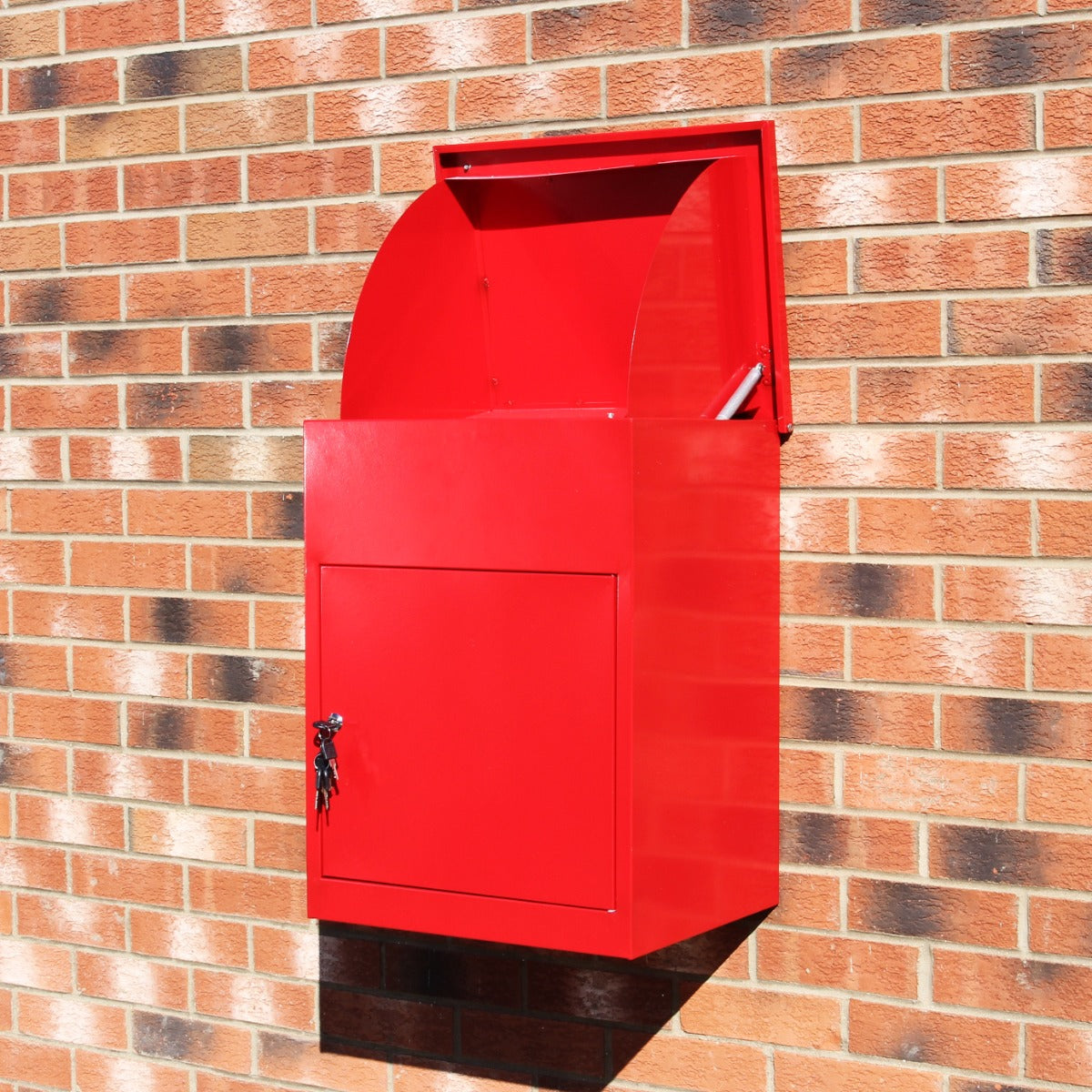 Roter Paketkasten aus Metall mit glatter Oberfläche, halbrunder Oberseite und abschließbarem Fach, montiert an einer Ziegelwand