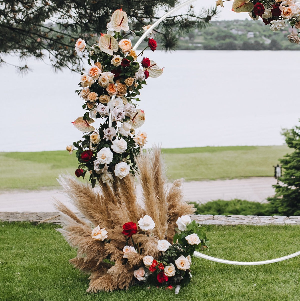 Hochzeit Ballonbogen in Weiß, dekoriert mit bunten Blumen, darunter Rosen und Trockenblumen, vor einer malerischen Landschaft am Wasser