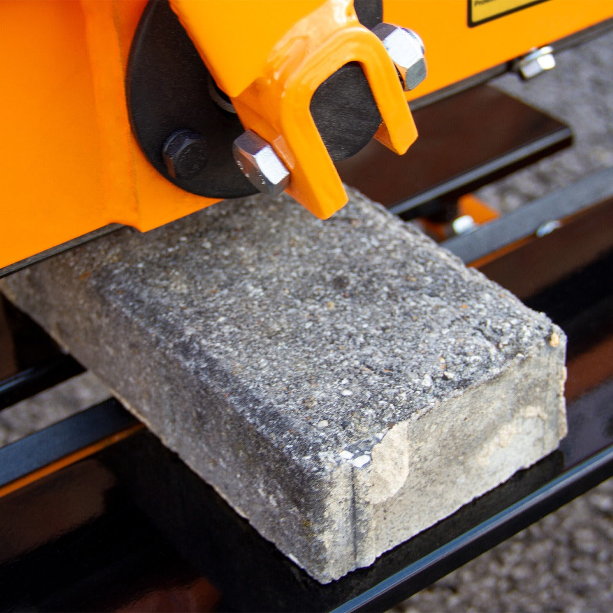 Der T-Mech 430mm Steinknacker zeigt einen grauen Betonblock unter einem orangefarbenen, robusten Schneidmechanismus mit Metallbefestigungen