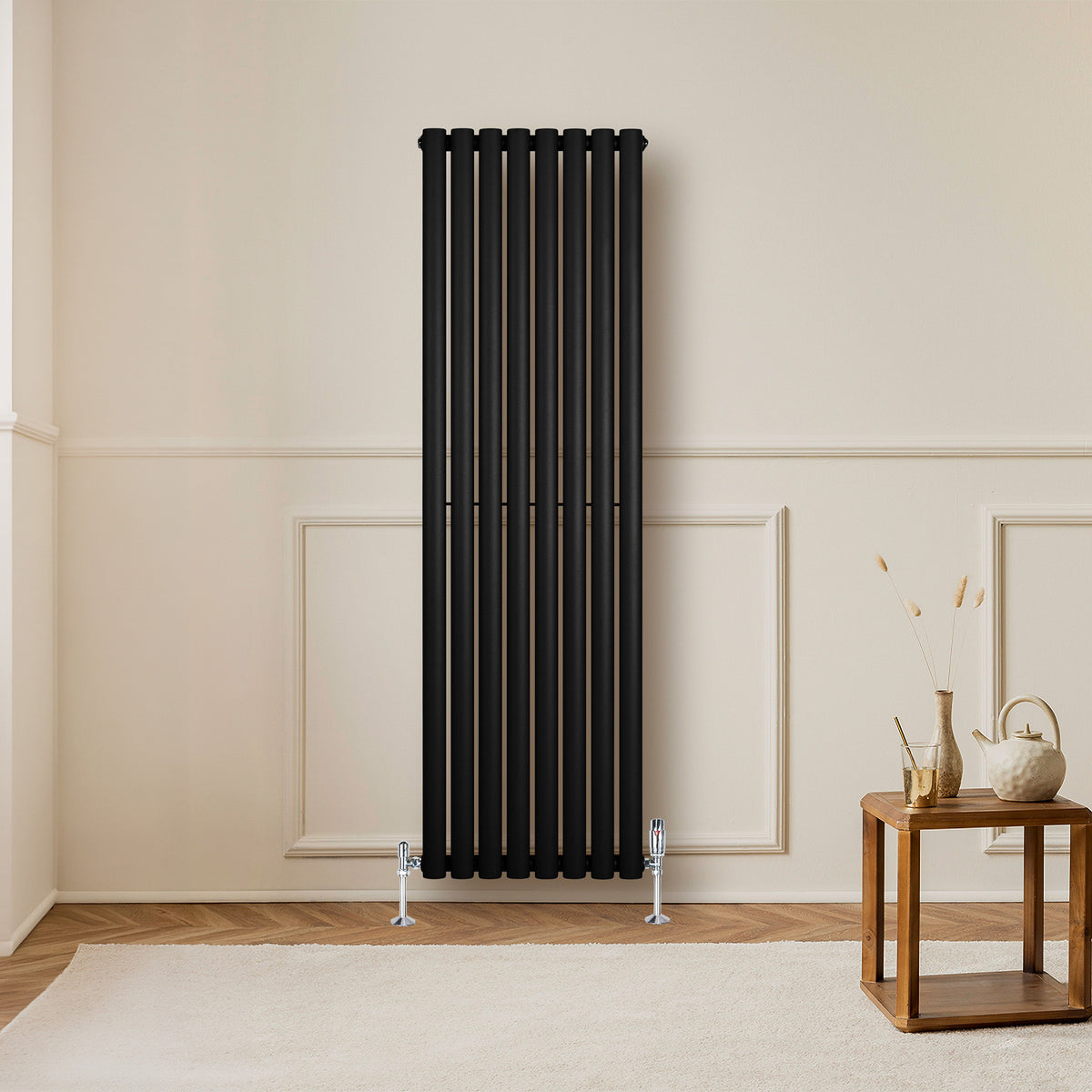 Schwarzer Gliederheizkörper mit TRV Chromventilen, 1600mm x 480mm, vertikal an einer hellen Wand montiert, umgeben von minimalistischer Raumgestaltung
