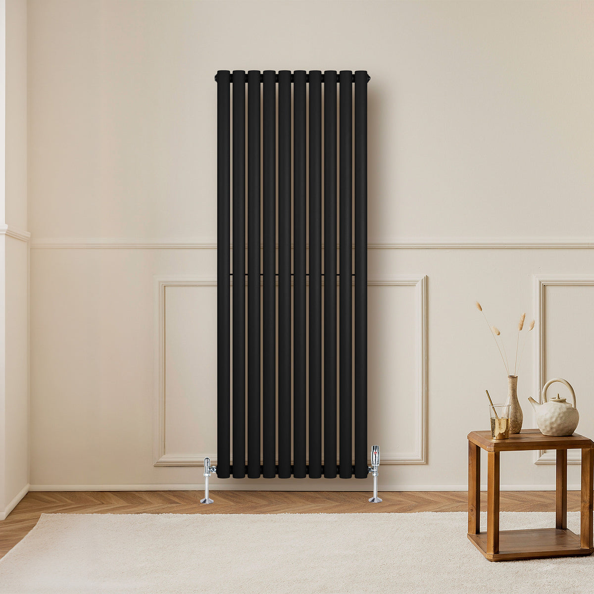 Schwarzer Gliederheizkörper mit TRV Chromventilen, 1600mm x 600mm, elegant an einer hellen Wand, ergänzt durch einen modernen Holztisch und Dekoration