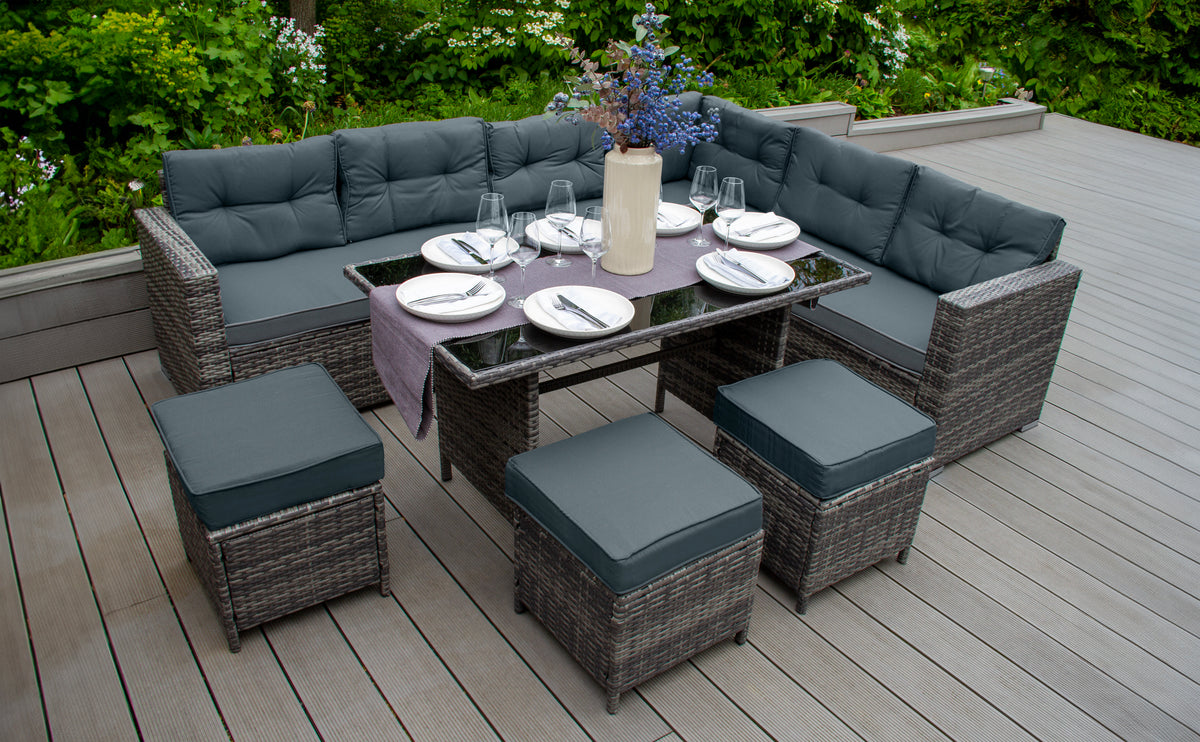 Elegantes Gartenmöbel-Set aus geflochtenem Rattan mit grauen Polstern, einem Tisch mit schwarzer Glasplatte und dekorativen Blumen in einer Vase