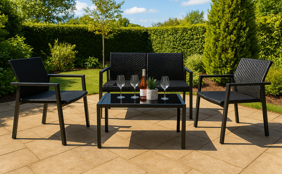 Schwarzes Gartenmöbelset mit zwei Stühlen und einem Tisch, umgeben von grünem Rasen und Bäumen, dekoriert mit Gläsern und einer Flasche Wein