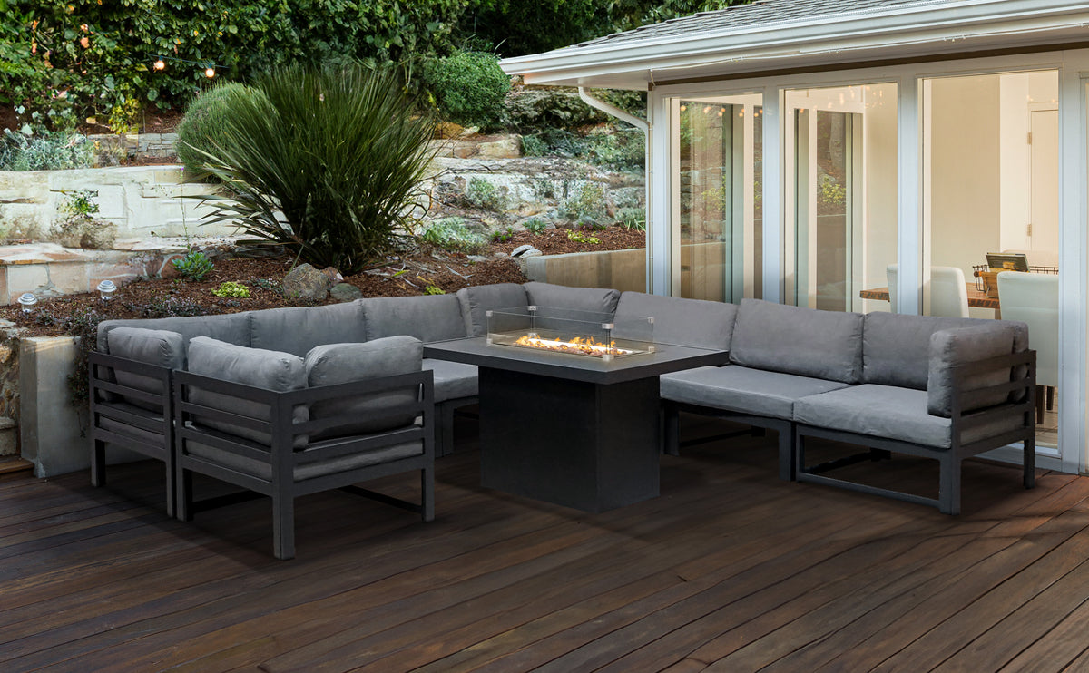 Moderne Gartenlounge mit grauem Polster und schwarzem Tisch, umgeben von Pflanzen und einem hellen Holzdeck, ideal für entspannte Abende