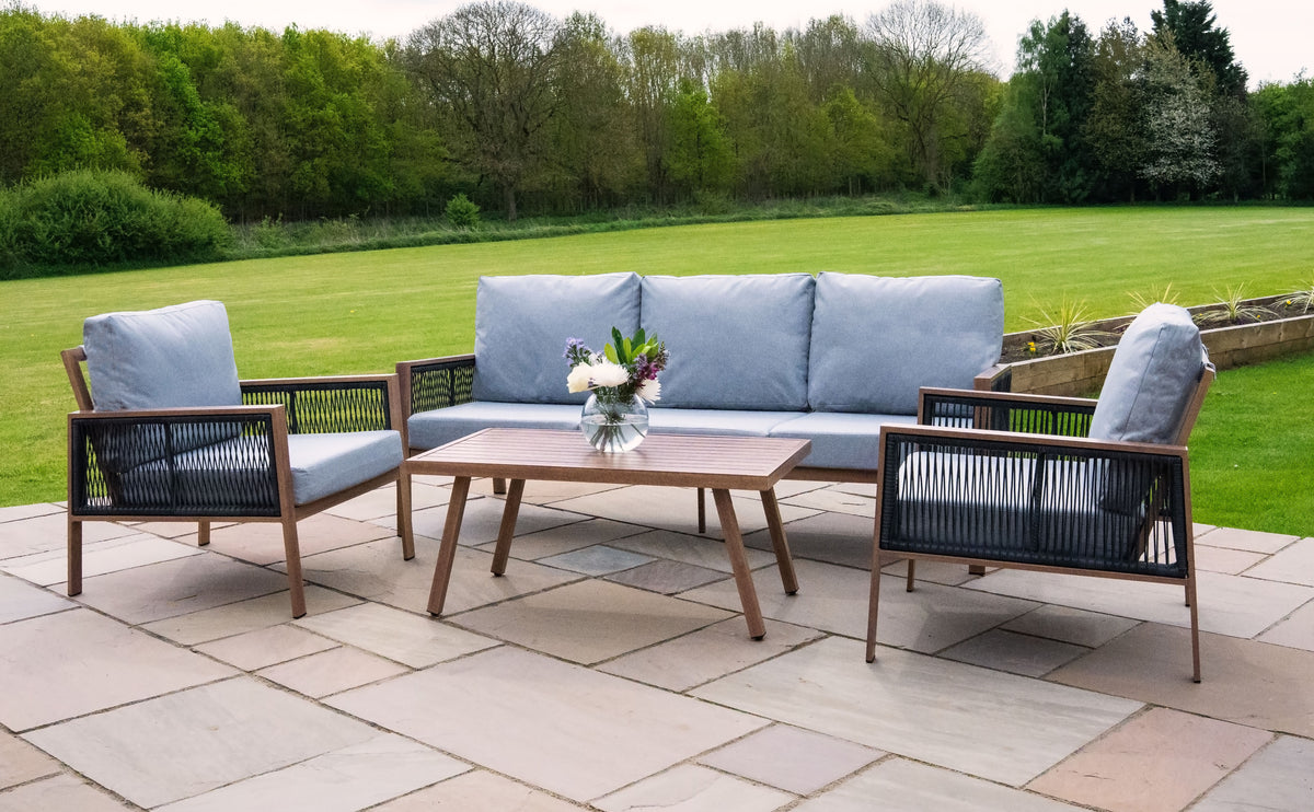 Elegantes Gartenmöbel-Set mit einem grauen Sofa und zwei Stühlen, kombiniert mit einem Holztisch, umgeben von einer grünen Wiese und Bäumen