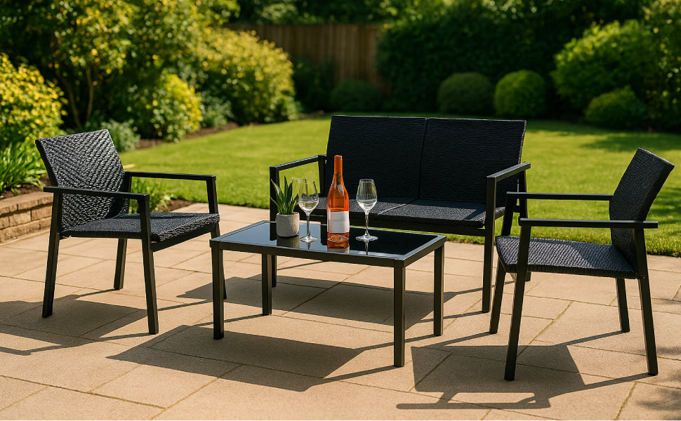 Schwarzes Gartenmöbelset aus Rattan mit zwei Stühlen und einer Couch, Tisch mit Weinflasche und Gläsern, umgeben von grünem Garten und Sonnenlicht