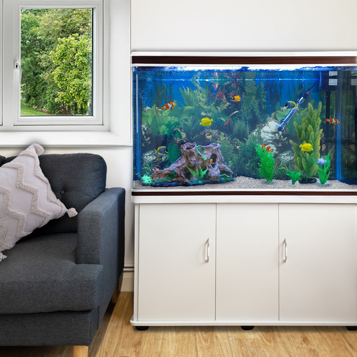 Weißes Aquarium Komplettset mit bunten Fischen, lebendigen Pflanzen und natürlichem Holz, platziert neben einem grauen Sofa und einem Fenster