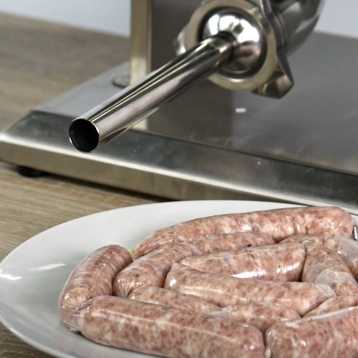 Kukoo Wurstfüller aus Edelstahl mit glänzendem Trichter, daneben ein Teller mit frisch gefüllten, appetitlichen Würsten in verschiedenen Größen