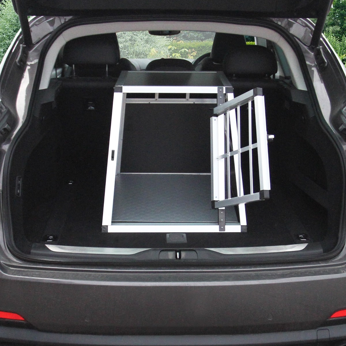Kleine Hundetransportbox aus robustem Aluminium und schwarzem Kunststoff, geöffnet im Kofferraum eines Autos, ideal für sichere Tiertransporte