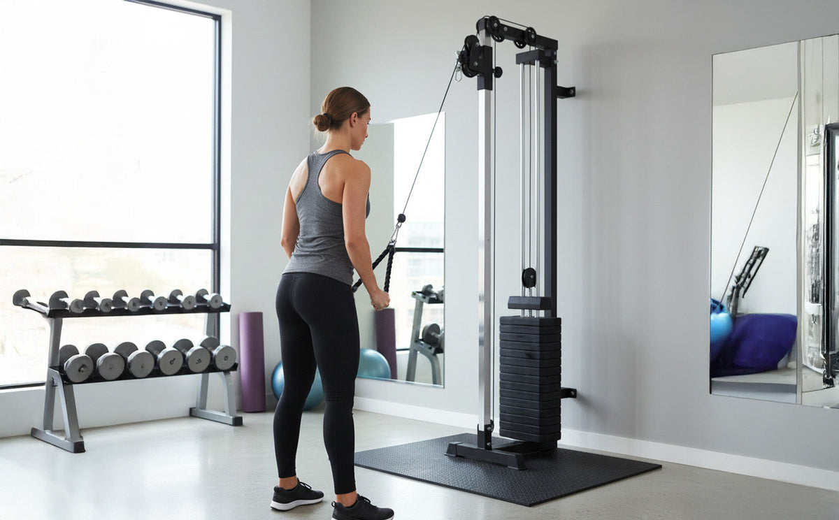 Frau in sportlicher Kleidung trainiert an einem kompakten Kabelzuggerät in einem modernen Fitnessstudio mit großen Fenstern und Gewichten im Hintergrund