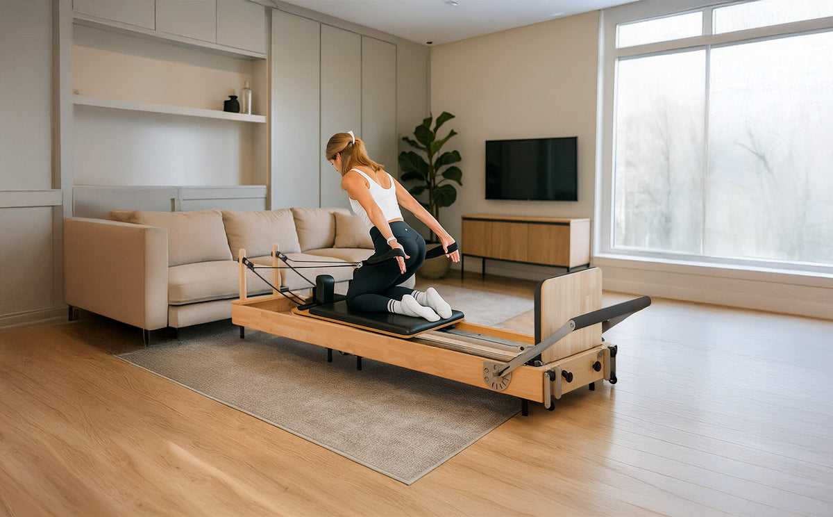 Moderne Pilates Reformer Maschine aus hellem Holz, mit einer sportlichen Frau in Schwarz, die eine Dehnübung im stilvollen Wohnzimmer ausführt