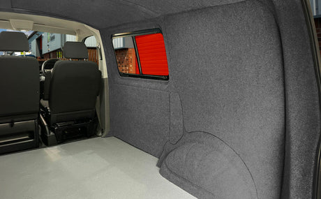 Dunkelgraue, weiche Verkleidung im Inneren eines Campervans, die eine gemütliche Atmosphäre schafft, mit gepolsterten Sitzen und einem großen Fenster