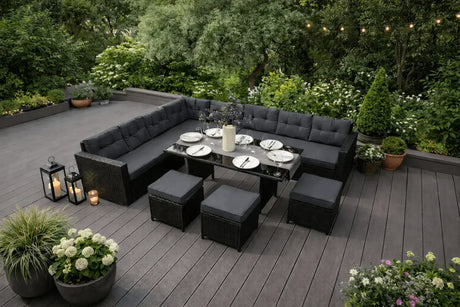 Elegantes, schwarzes Gartenmöbelset mit gepolsterten Sitzen, einem gläsernen Tisch und stilvollen Laternen, umgeben von üppigem Grün und blühenden Pflanzen