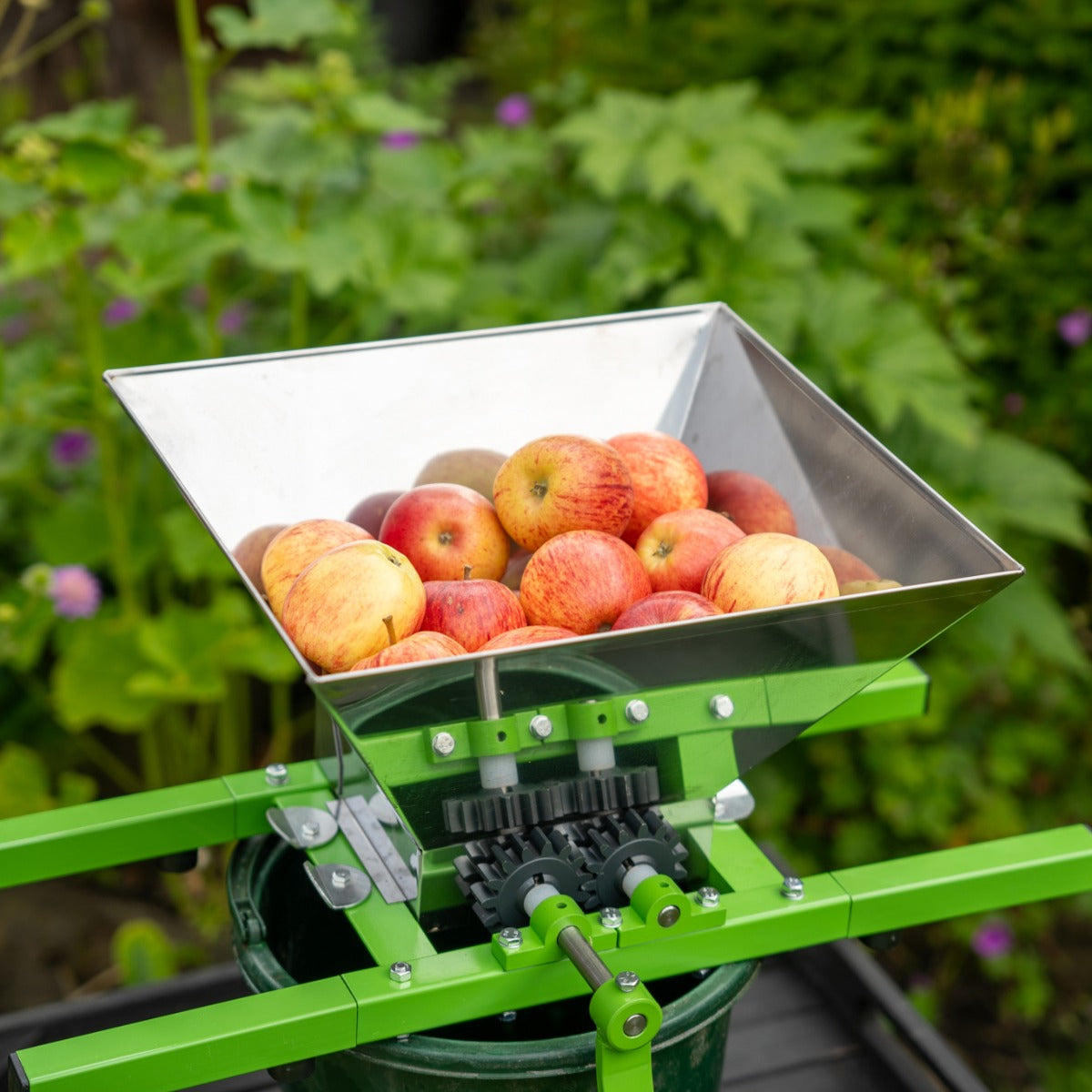Edelstahl Obstpresse mit grünem Gestell, gefüllt mit roten Äpfeln, ideal zum Saftpressen und Zerkleinern von Obst im Garten