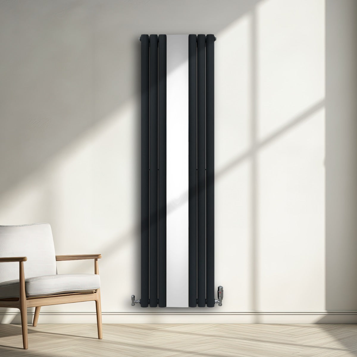 Ovaler Röhrenheizkörper in Anthrazitgrau mit integriertem Spiegel und Chrom-Thermostatventilen, elegant an einer hellen Wand montiert, neben einem modernen Stuhl