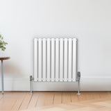 Ovaler Röhrenheizkörper in Weiß mit Chrom-Thermostatventilen, 600mm x 600mm, an einer hellen Wand, auf einem Holzfußboden platziert