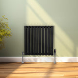 Schwarzer ovaler Röhrenheizkörper mit Chrom-Thermostatventilen, 600mm x 600mm, vor einer hellgrünen Wand und Holzfußboden, modern und elegant