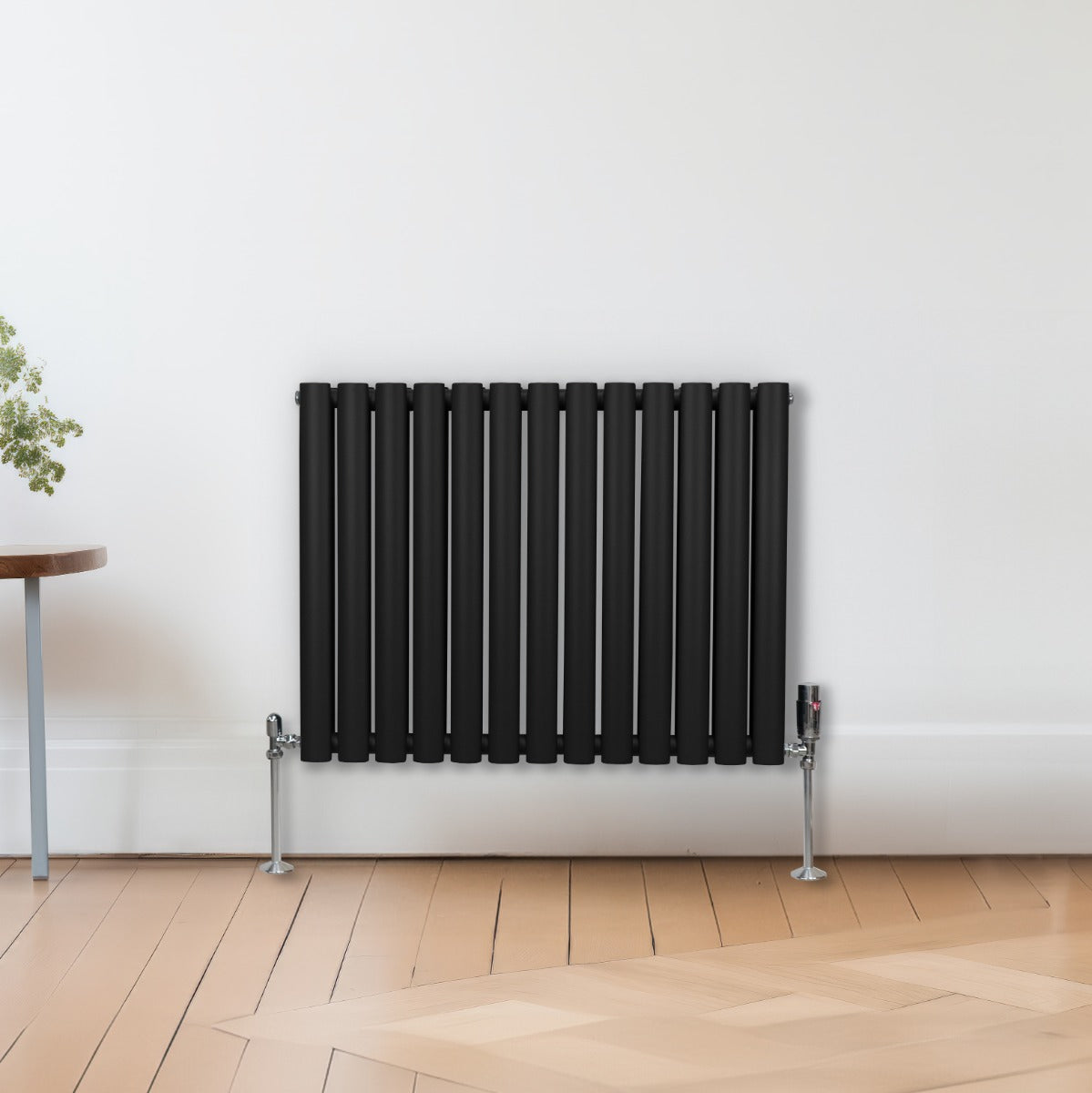 Schwarzer ovaler Röhrenheizkörper mit Chrom-Thermostatventilen, 600mm x 780mm, an einer hellen Wand, Holzfußboden, modern und elegant